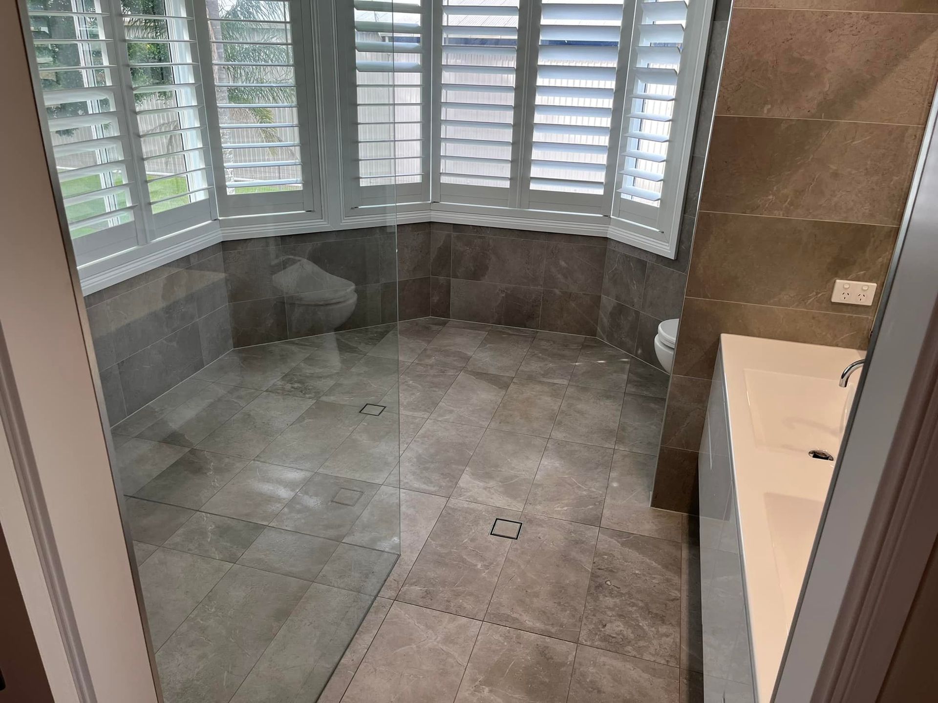 Bathroom with gray tiled floor, a window with white shutters, and a white sink — JNR Building And Maintenance in Green Hill, QLD