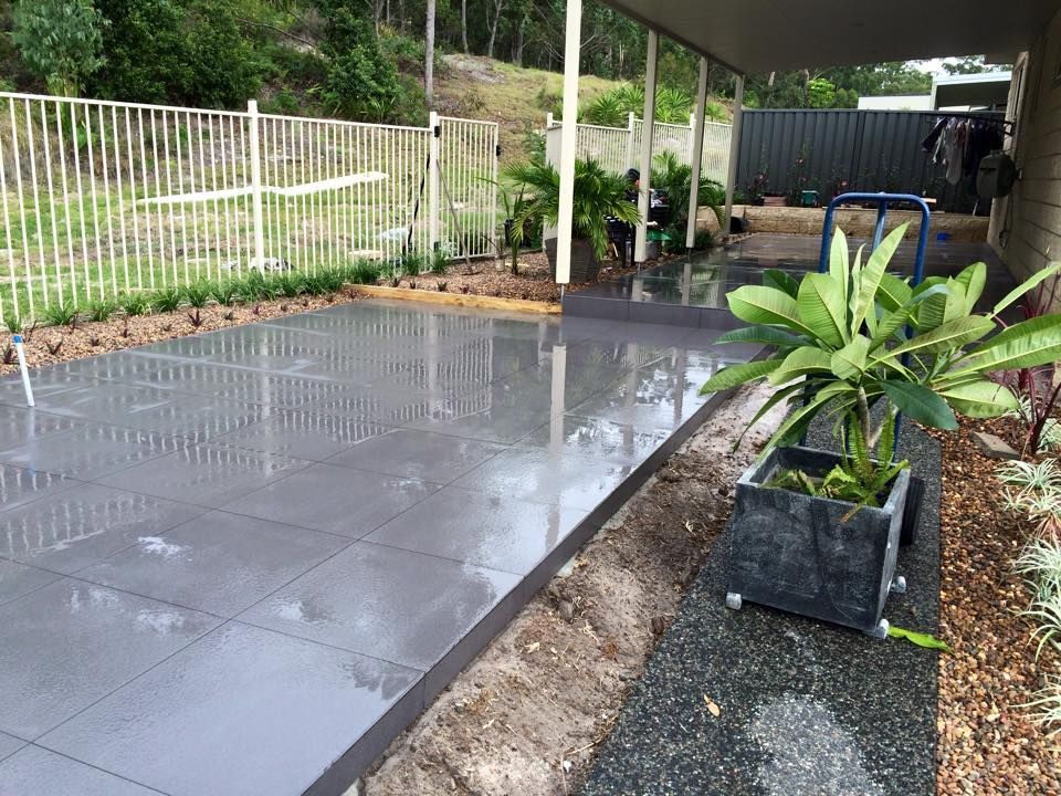 Wet Gray Tiled Patio Next to a Garden Bed and Fence  — JNR Building And Maintenance in Green Hill, QLD
