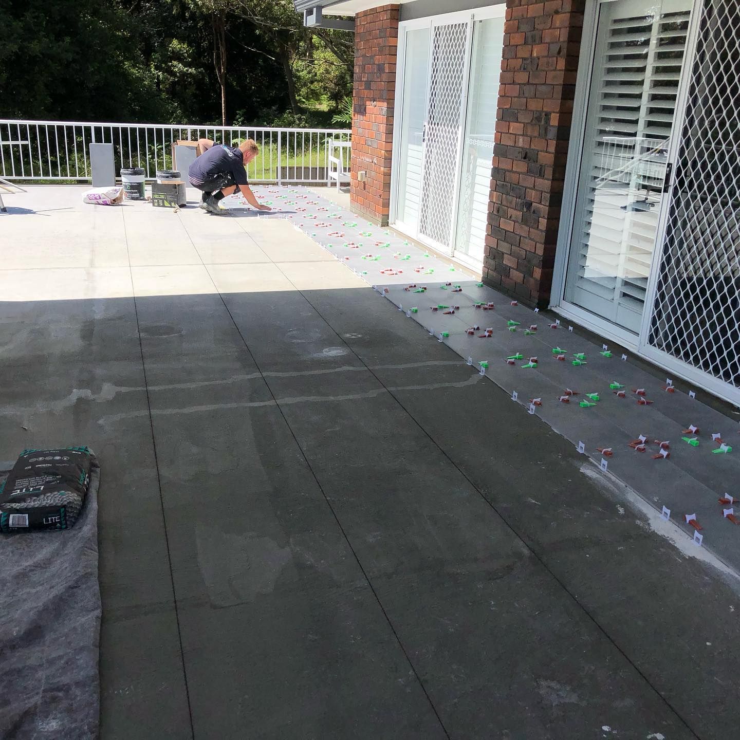 Person Tiling a Patio With Gray Tiles, Near Glass Sliding Doors — JNR Building And Maintenance in Green Hill, QLD