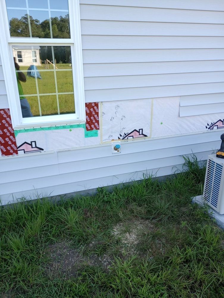 Exterior wall of a house with missing siding, revealing white foam insulation boards and a section of a window.
