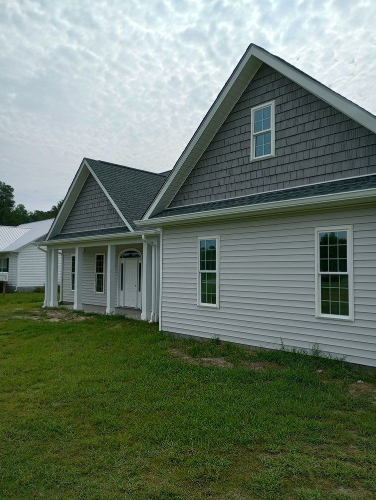 A new one-story house with light grey siding, dark grey shingles on the gables, a covered porch, and white trim.