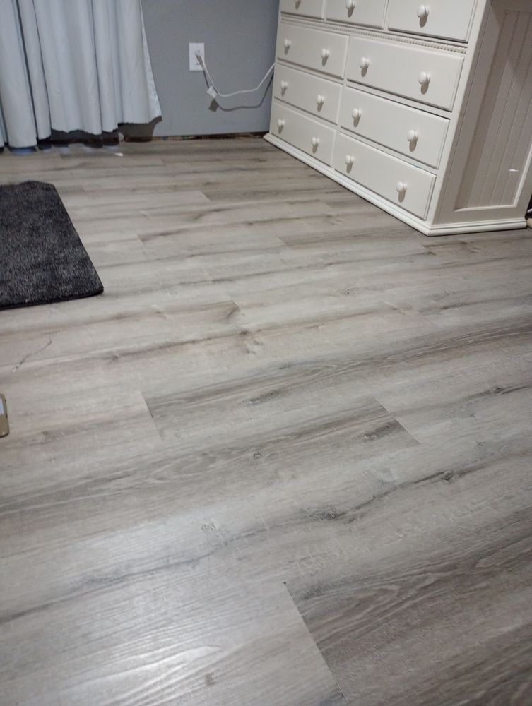 Light-colored wood-look laminate flooring in a room with a white dresser and a dark rug.
