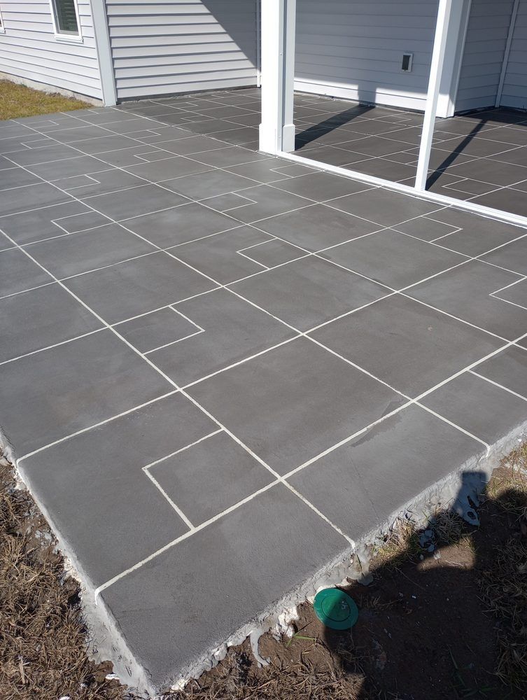 Gray concrete patio with a grid pattern of white lines and scattered, smaller square accents.