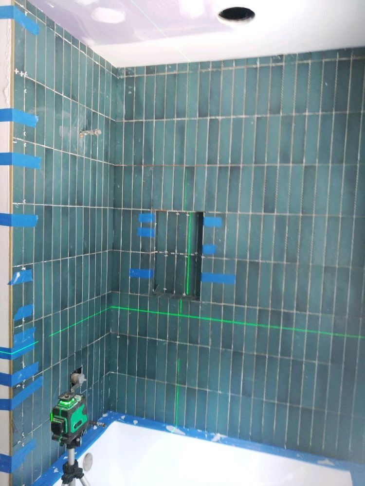 A green-tiled shower stall under construction with a laser leveling tool set up on a tripod.