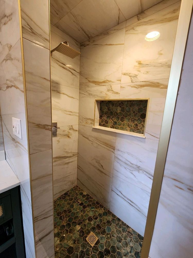 A modern shower with white marble-vein walls, a pebble-stone floor, a gold-framed niche, and a gold showerhead.