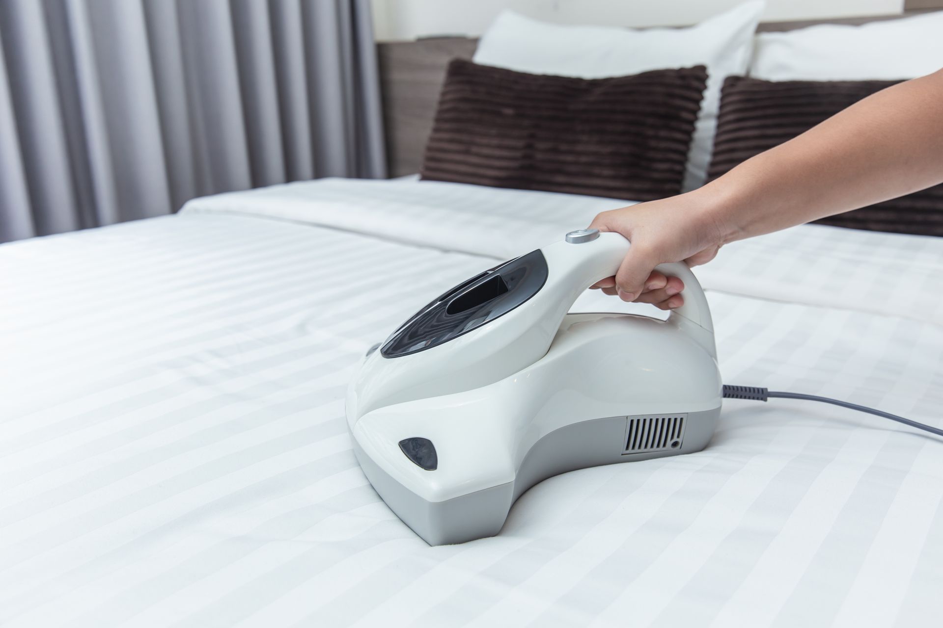 A person is using a vacuum cleaner to clean a bed.