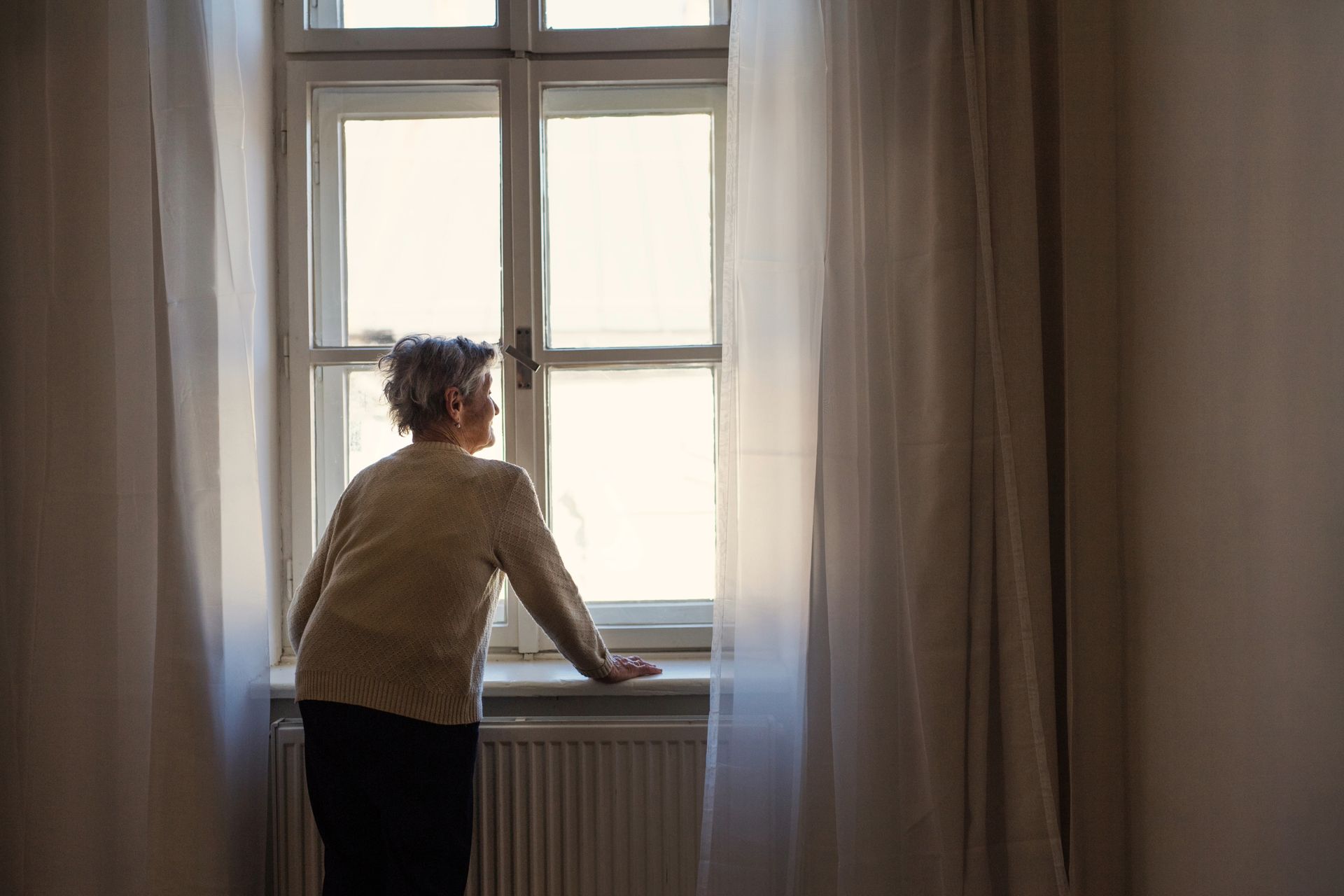 Person looking out a window with white curtains.