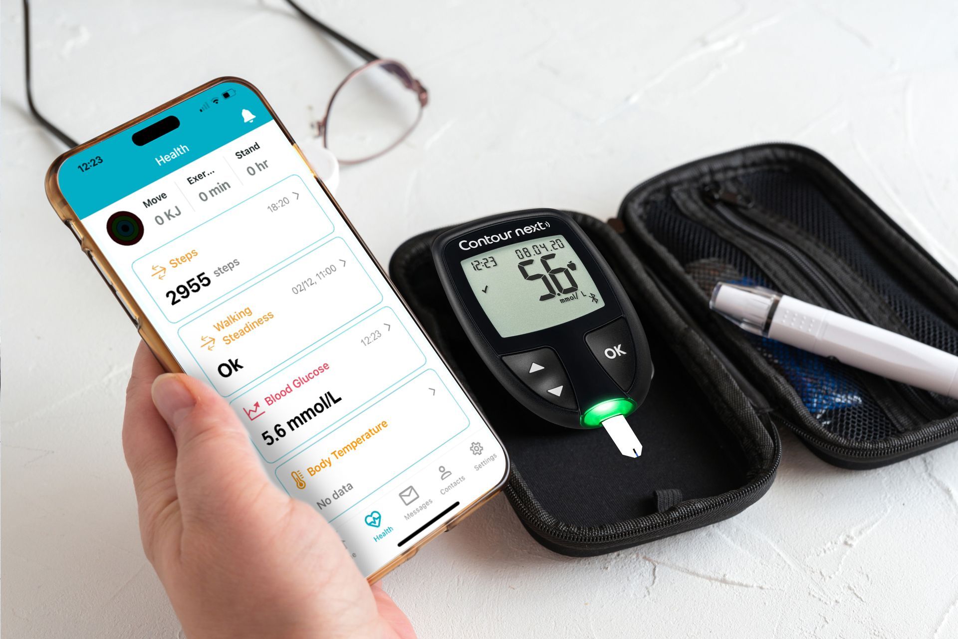 Person holding phone displaying health app data next to a blood glucose meter, case, and glasses.