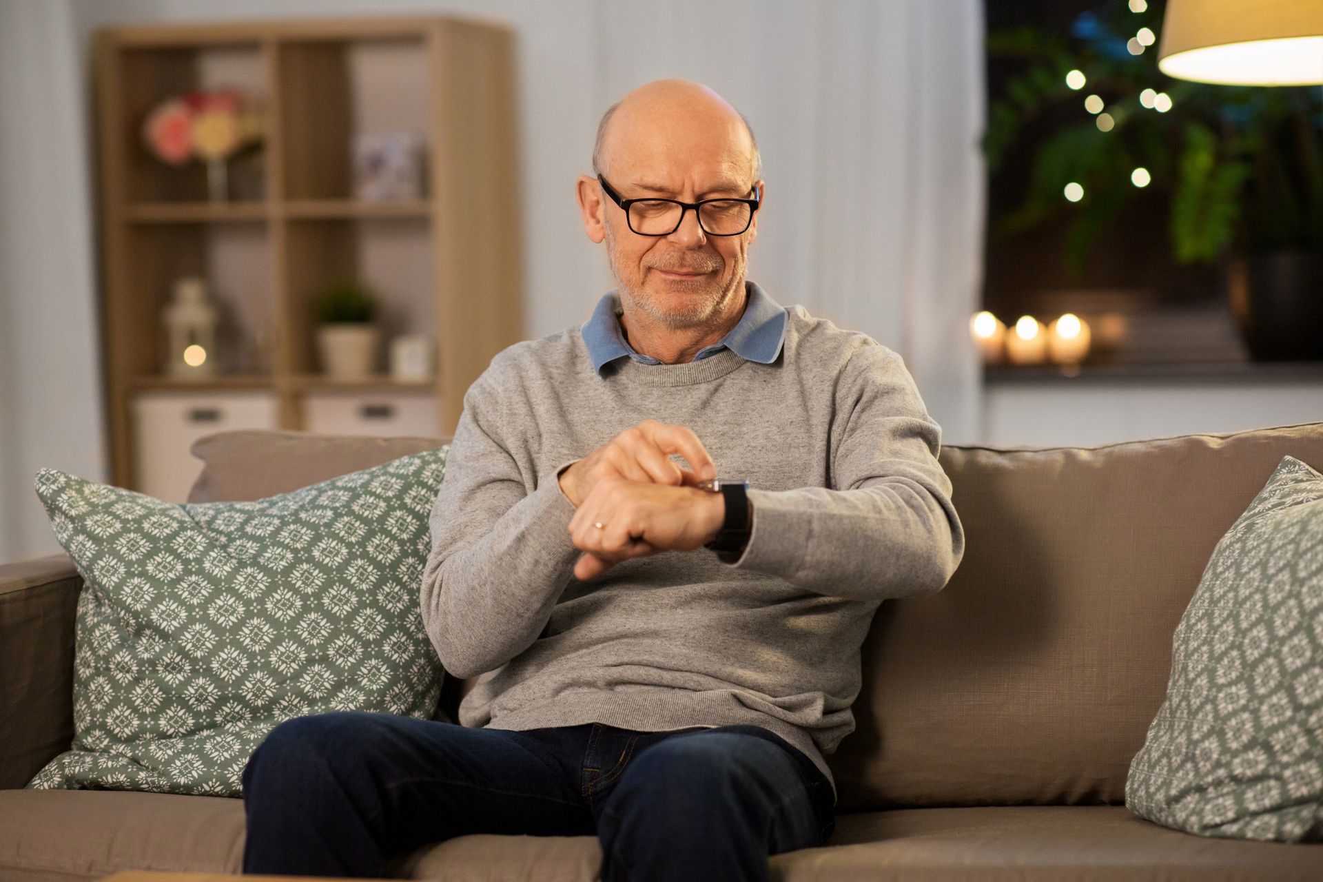 Man in glasses checks his smartwatch while seated on a sofa.