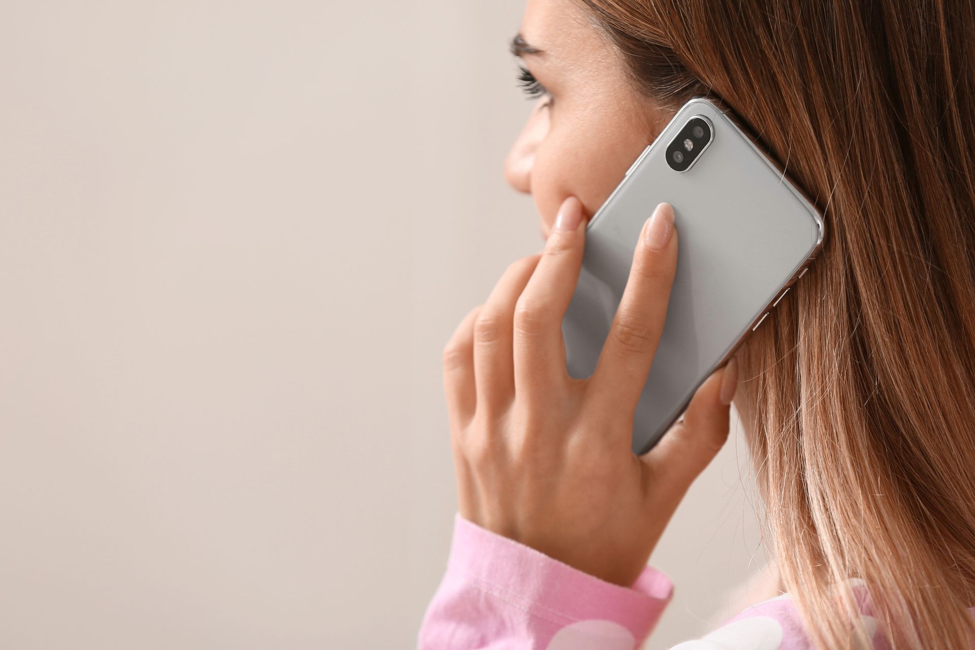 Woman holding a silver smartphone to her ear, close-up, beige background.