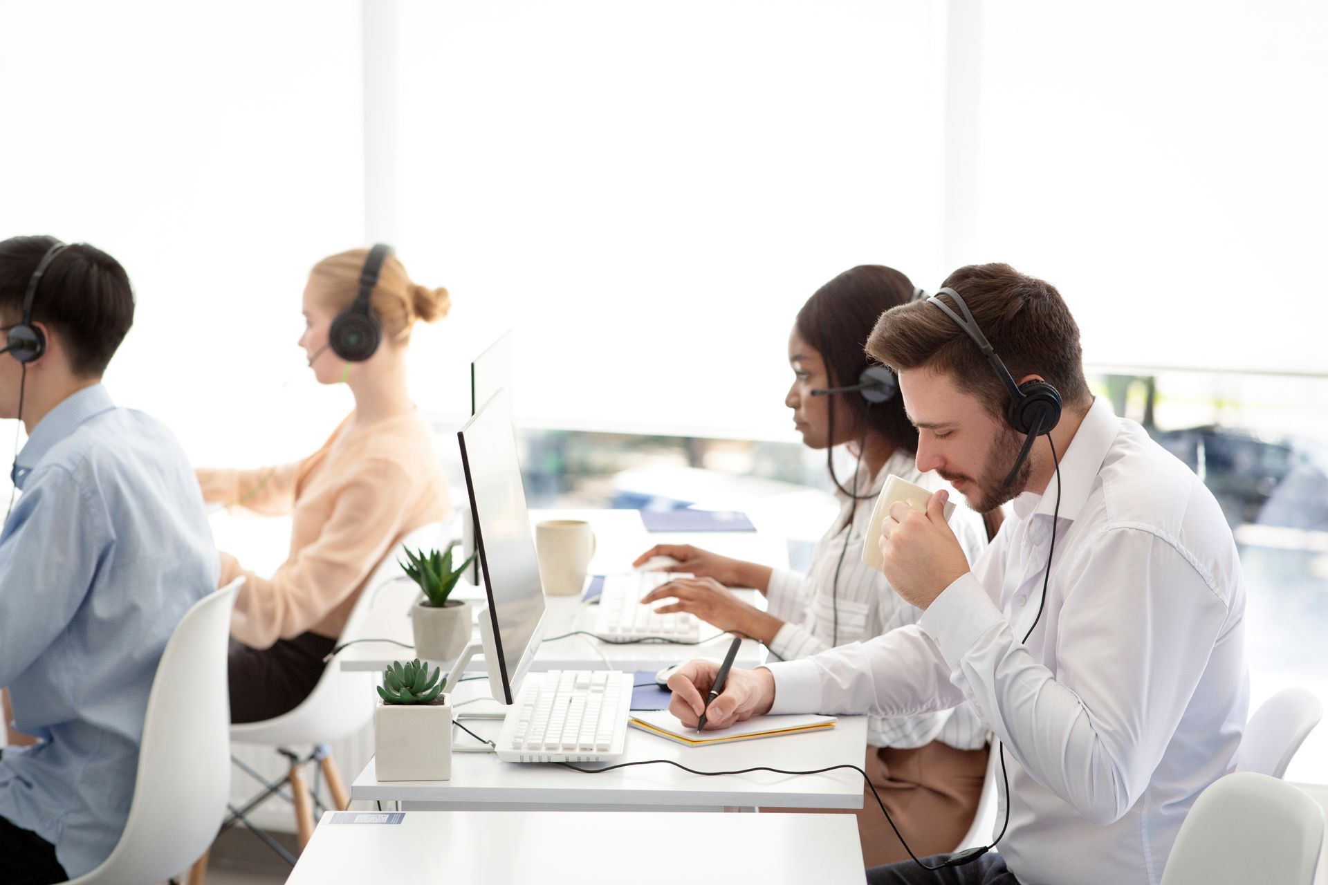 A group of people wearing headsets are sitting at desks in a call center.