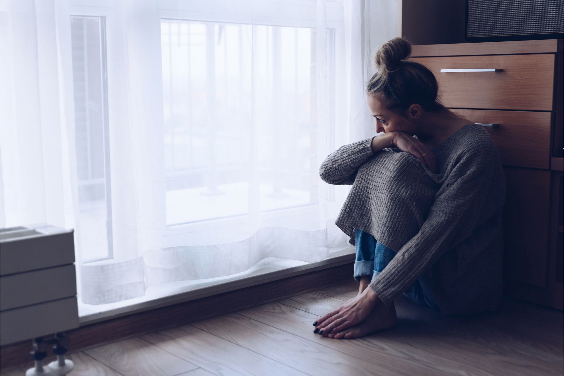 A woman is sitting on the floor in front of a window.