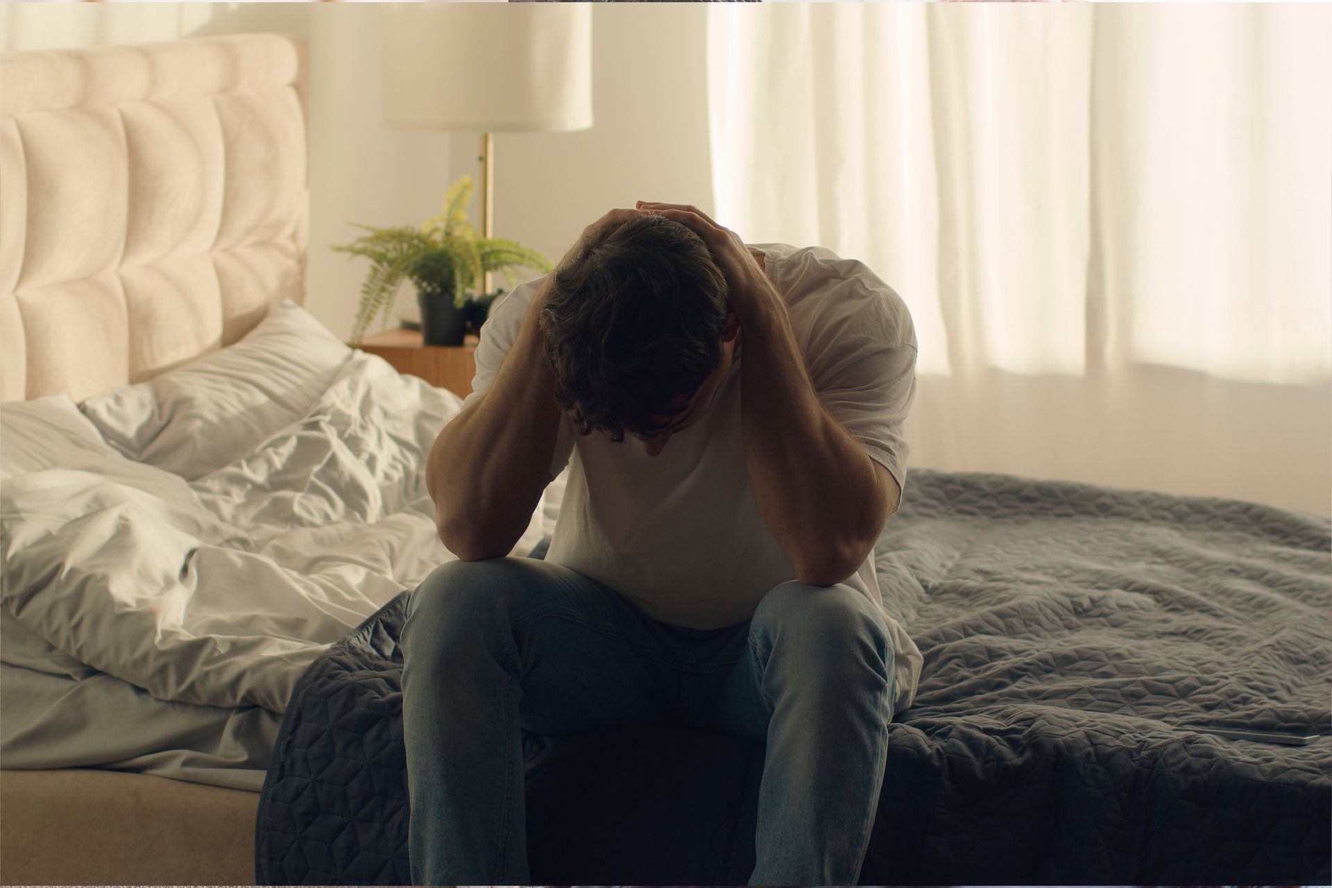 A man is sitting on a bed with his head in his hands.