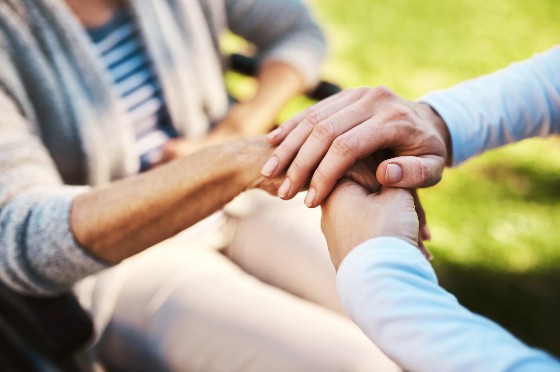 Hands holding, one person in a wheelchair. Outdoors.