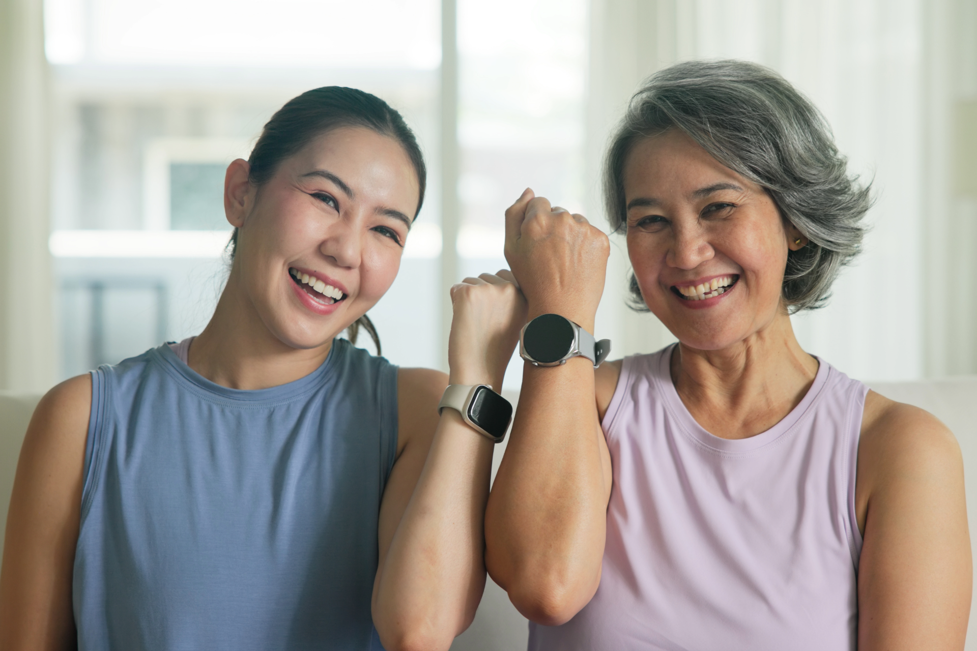 Two women are sitting on a couch holding hands and wearing smart watches.