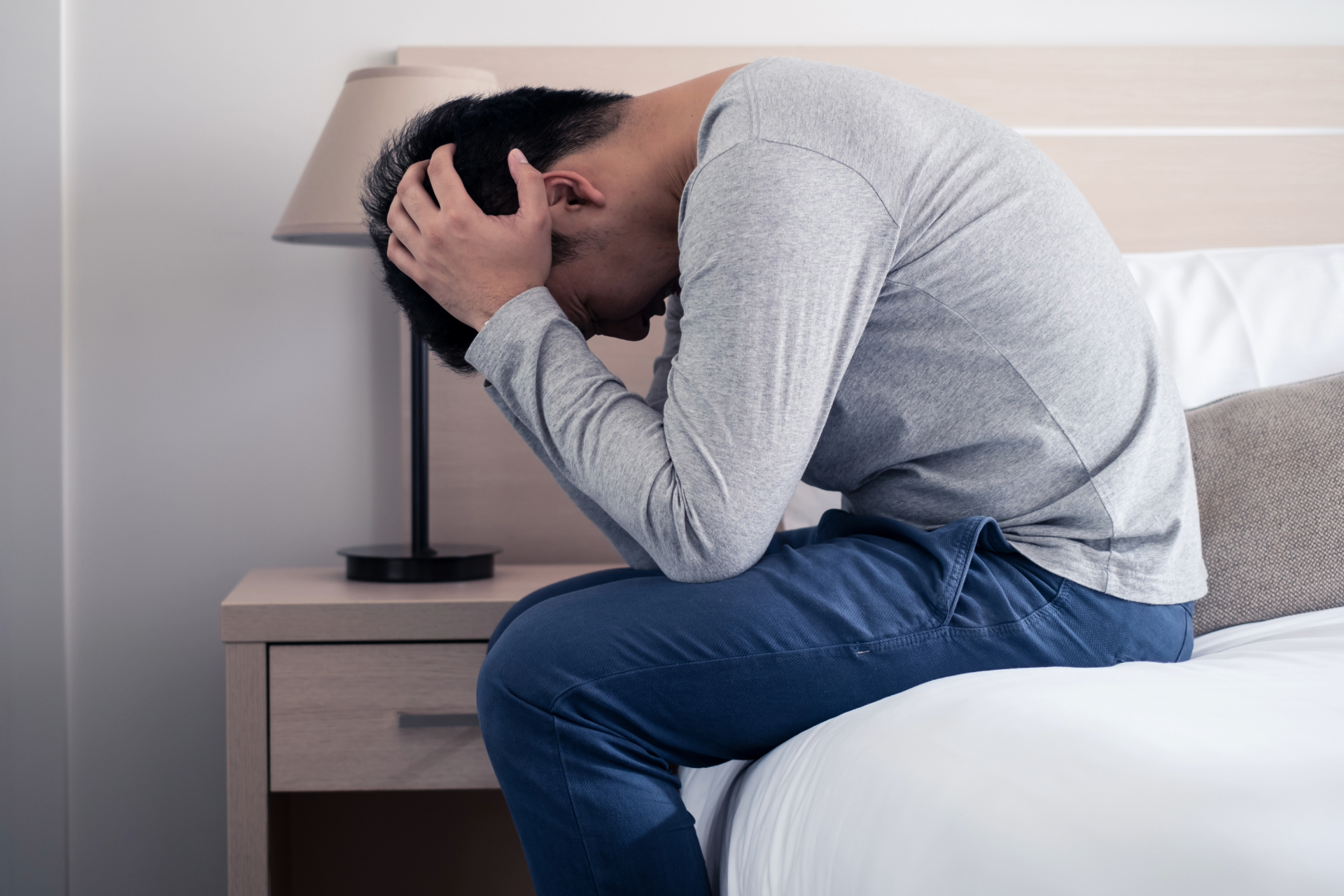A man is sitting on a bed with his head in his hands.