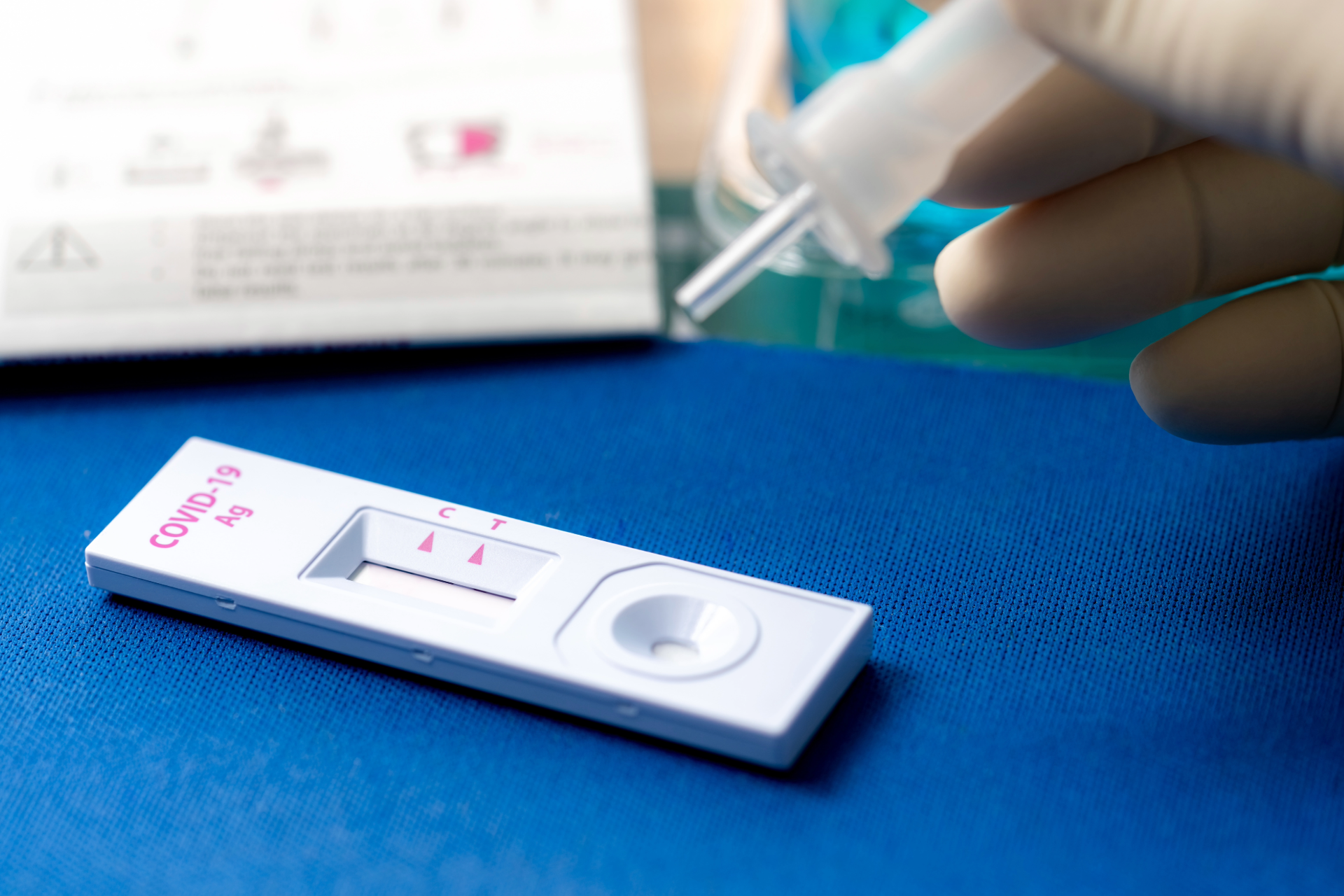 A person is holding a syringe over a covid-19 test kit.