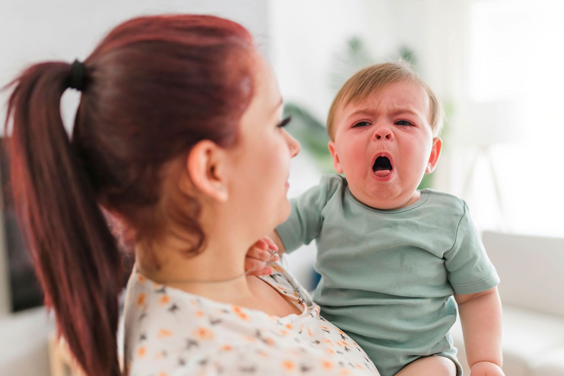 A woman is holding a crying baby in her arms.