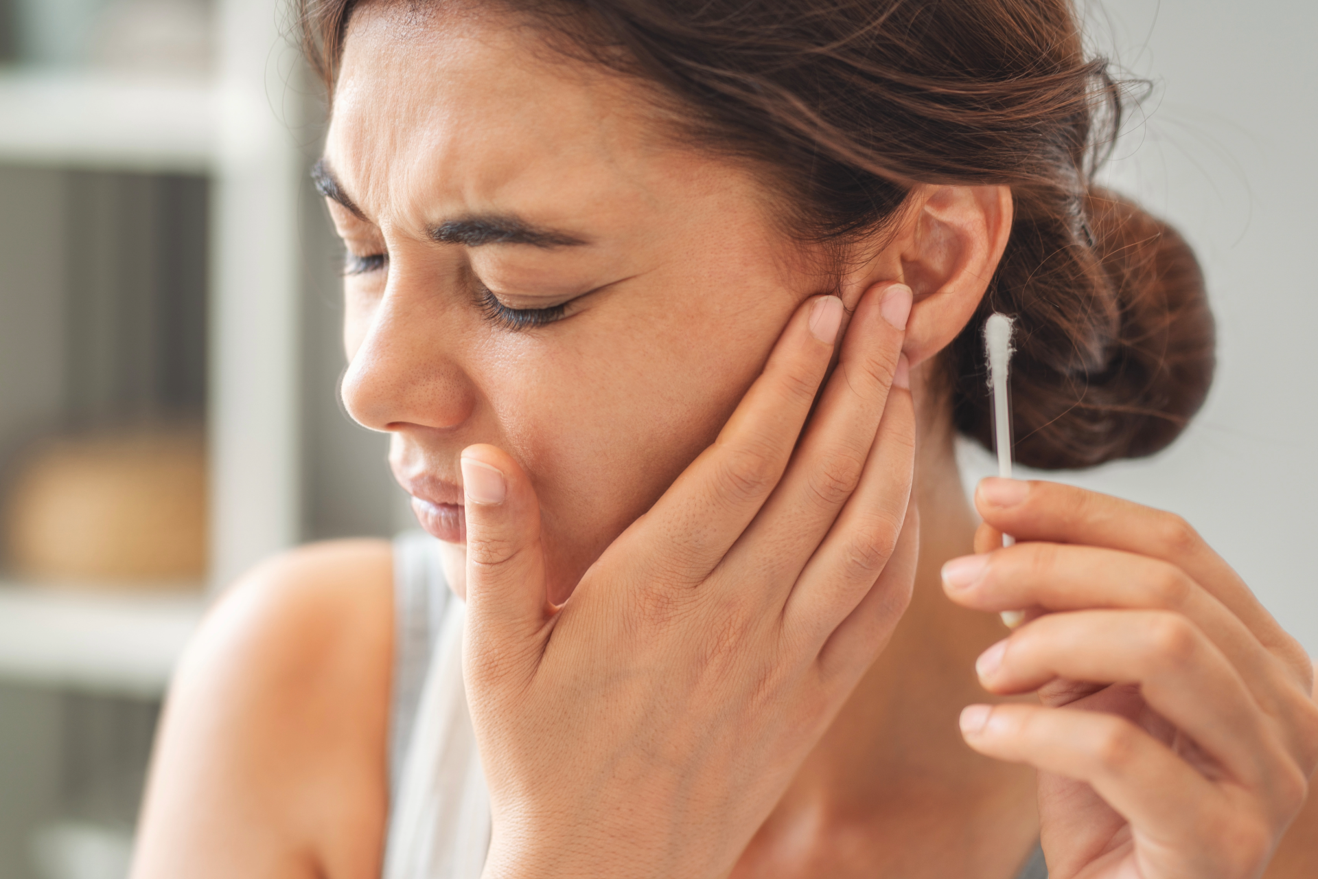 A person holds a cotton swab to their ear while grimacing in pain, suggesting ear discomfort.