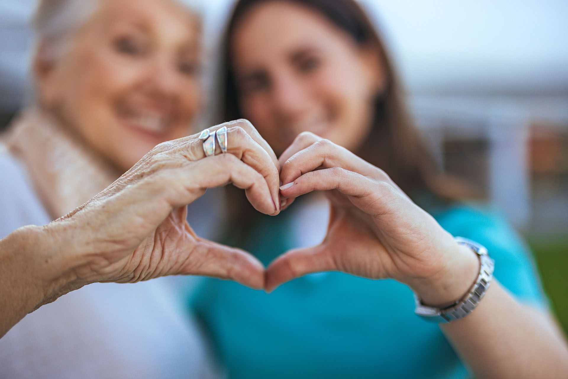 An elderly woman and a young woman are making a heart shape with their hands.