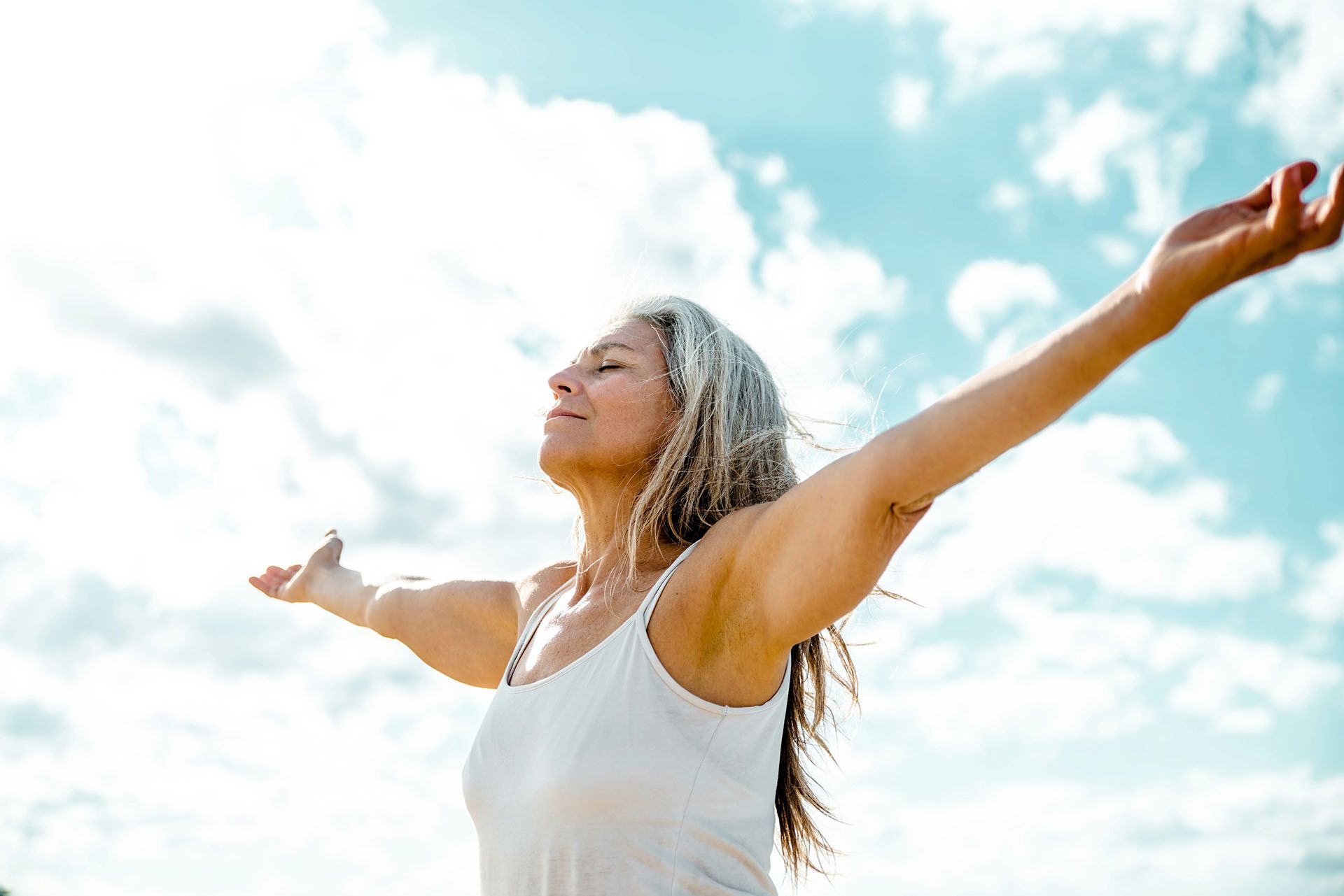 A woman is standing with her arms outstretched in front of a blue sky.