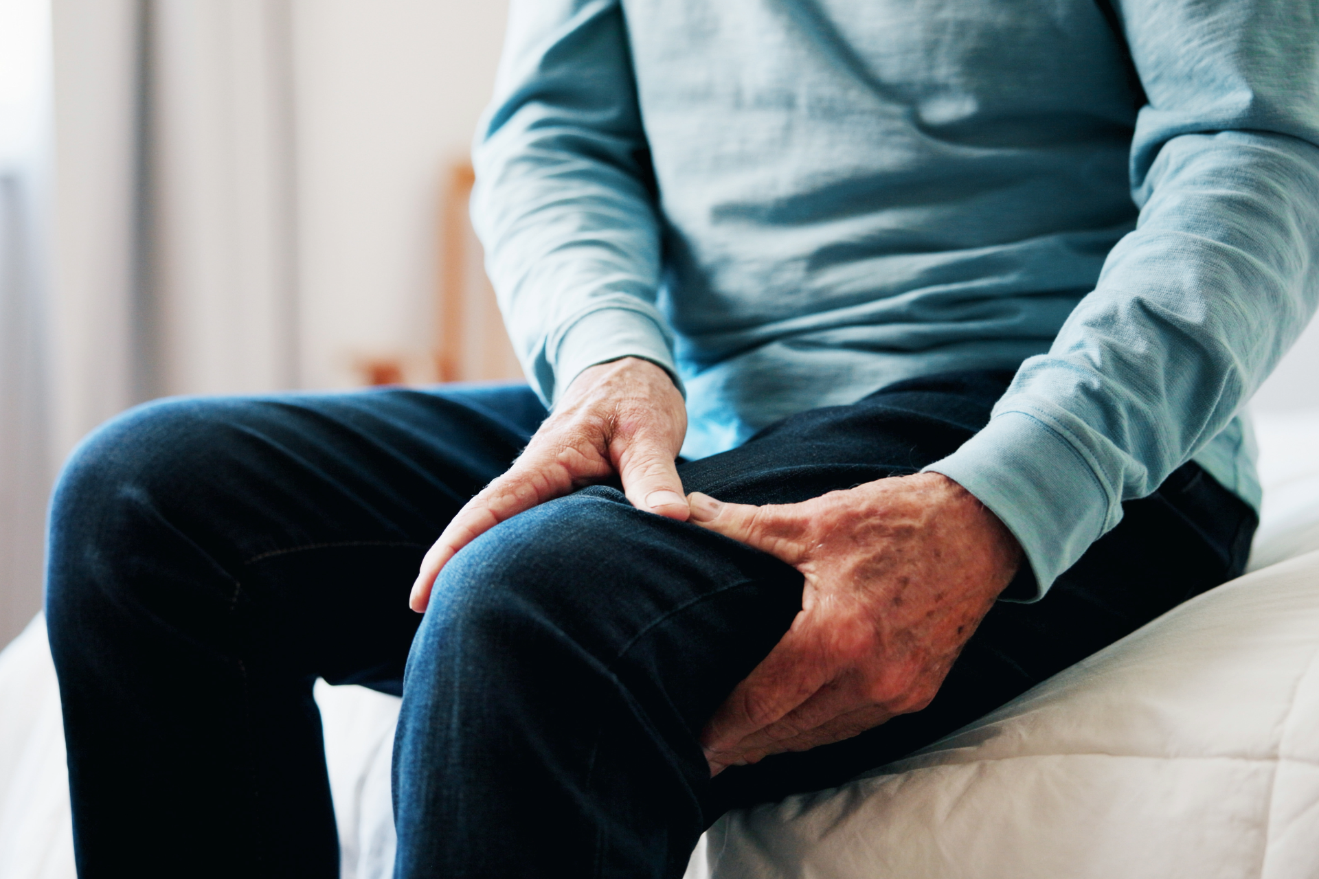 Person sitting on a bed holding their thigh with both hands.