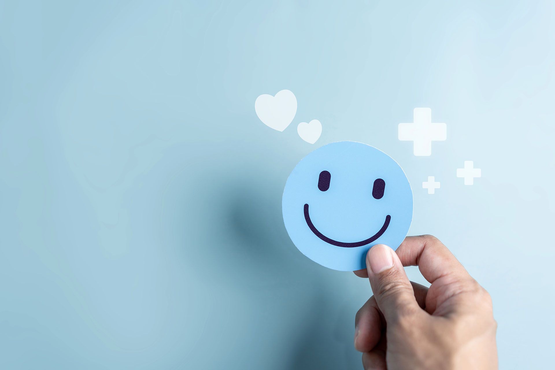 A person is holding a paper smiley face with hearts and crosses around it.