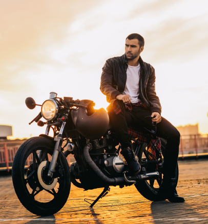 Man in leather jacket sits on a black motorcycle, golden sunset in background.