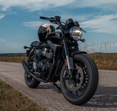 Black motorcycle parked on a paved road, helmet on seat; blue sky in the background.