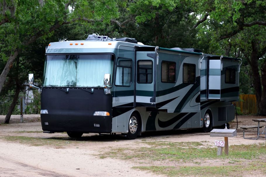 Large gray and black RV parked on a dirt lot among trees