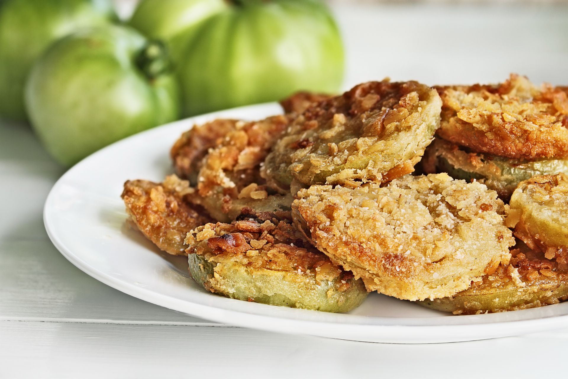 Plate of breaded fried green tomatoes with whole green tomatoes in the background