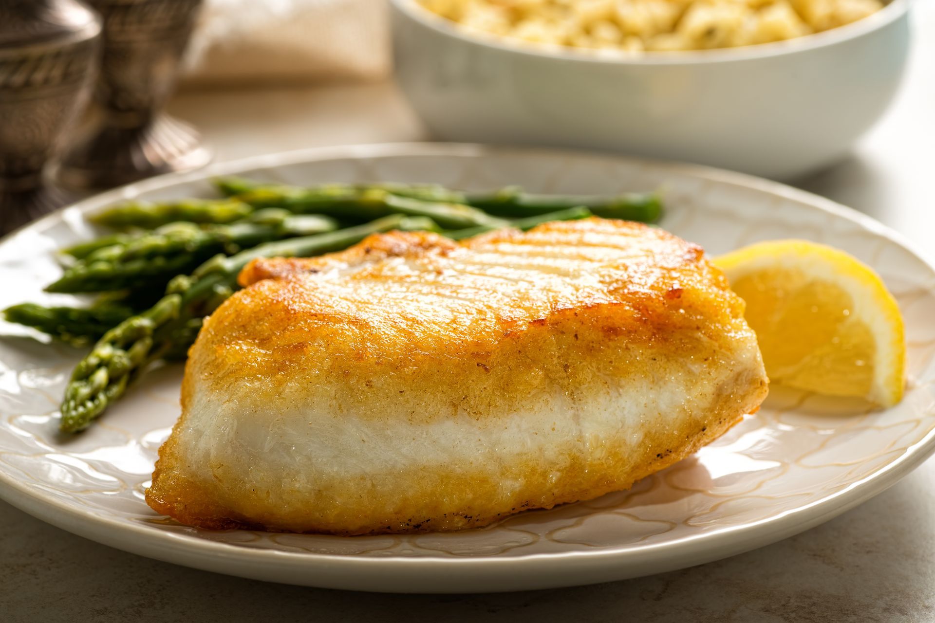 Grilled fish fillet with asparagus and lemon wedge on a white plate