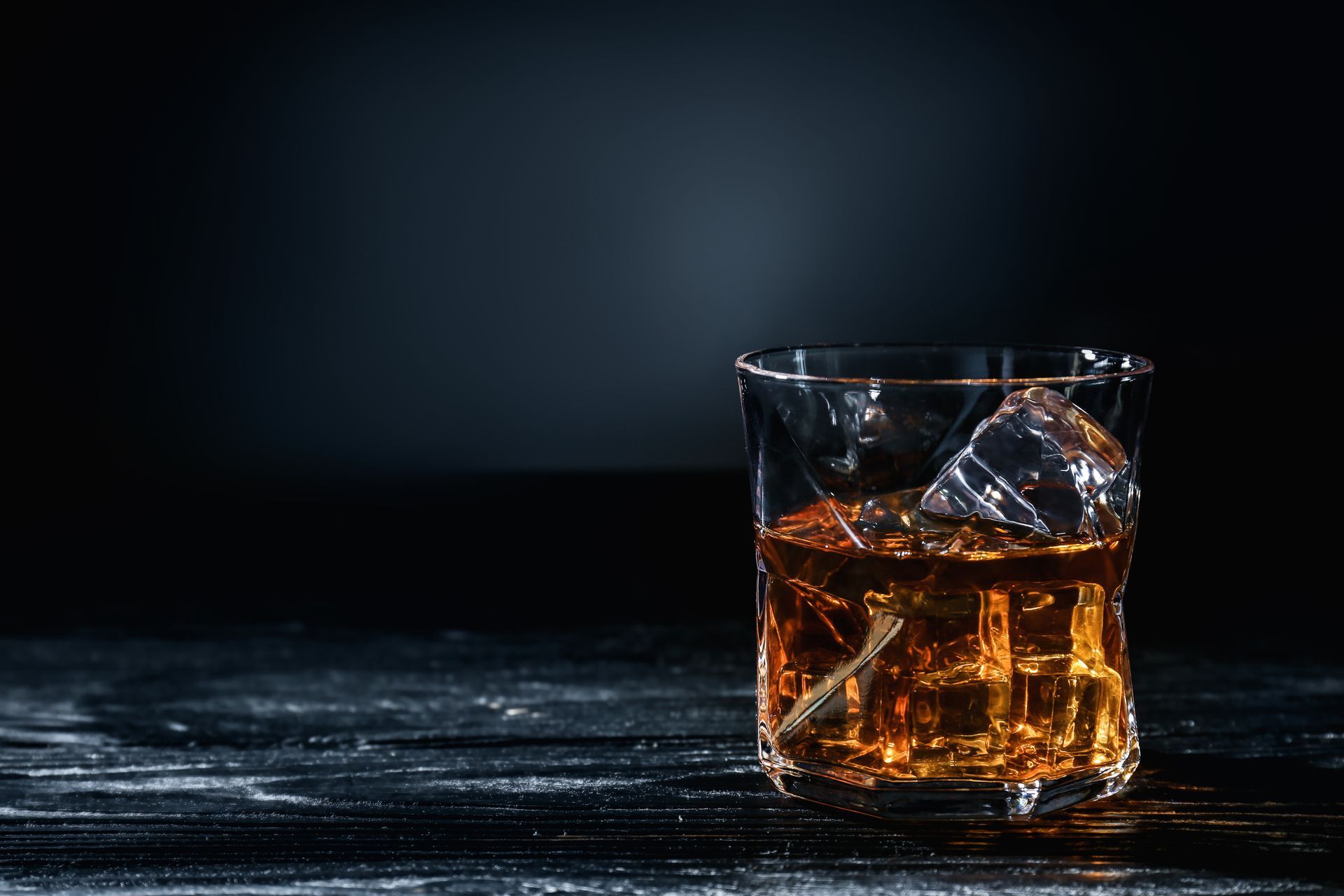 Whiskey glass with ice on a dark wooden table against a dark background