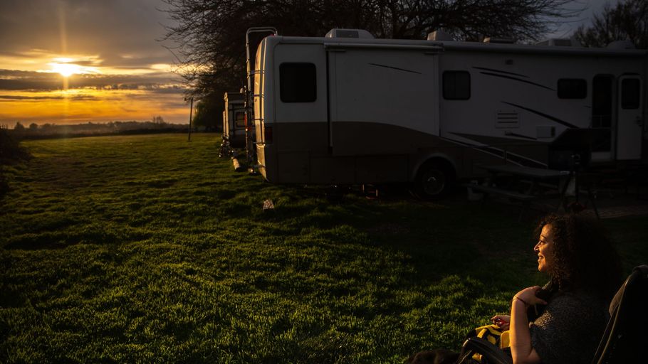 Sunset over a grassy campsite with an RV and a seated person in the foreground