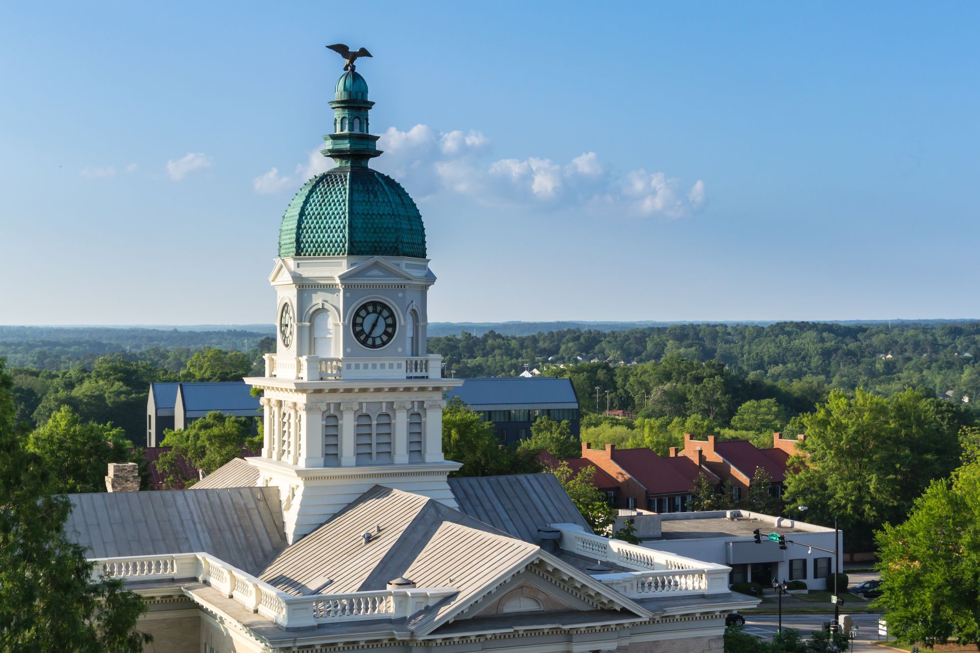 White domed clock tower with green roof rising above trees under a blue sky
