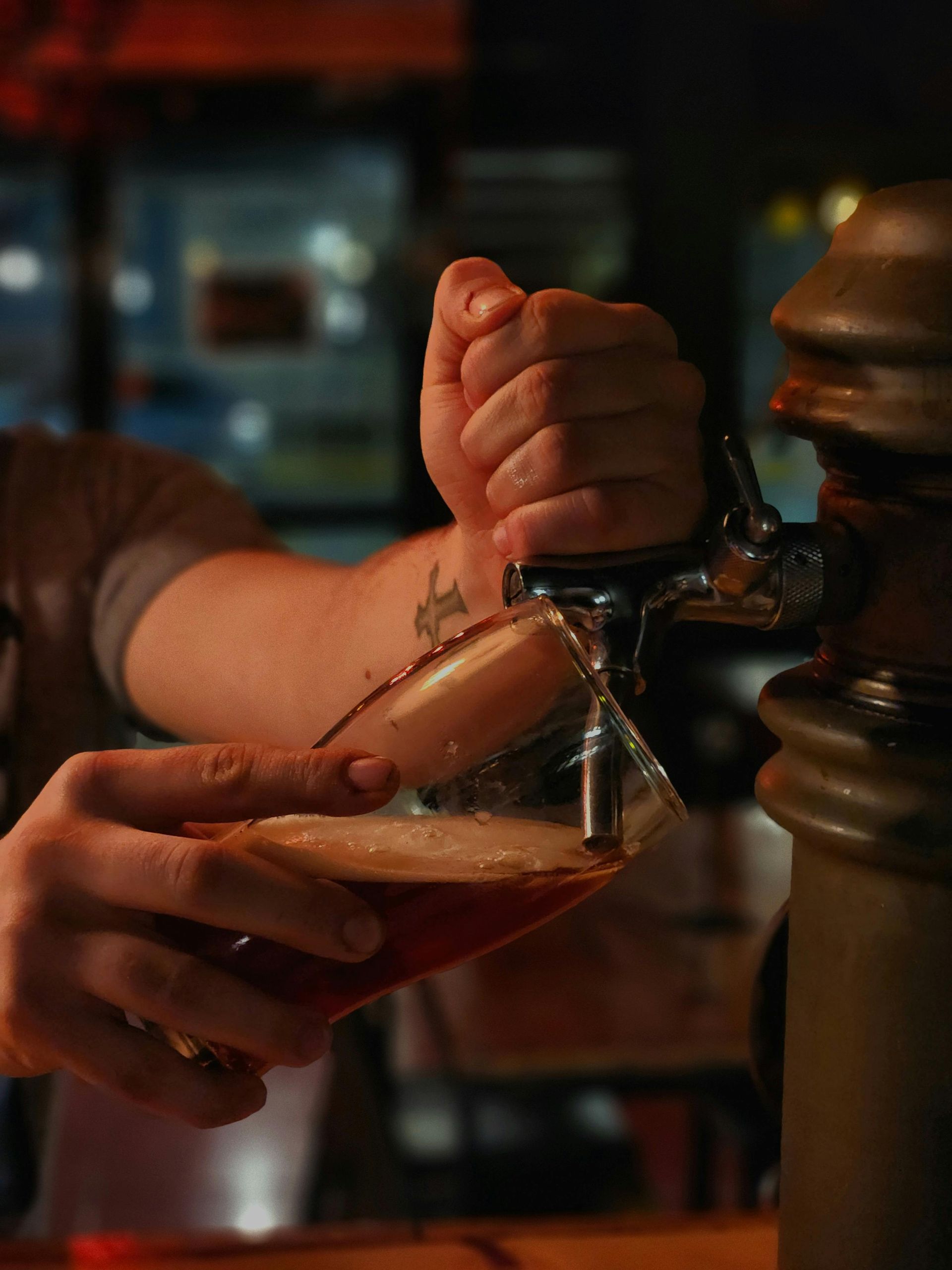 Hand pouring beer from a tap into a glass in a dimly lit bar