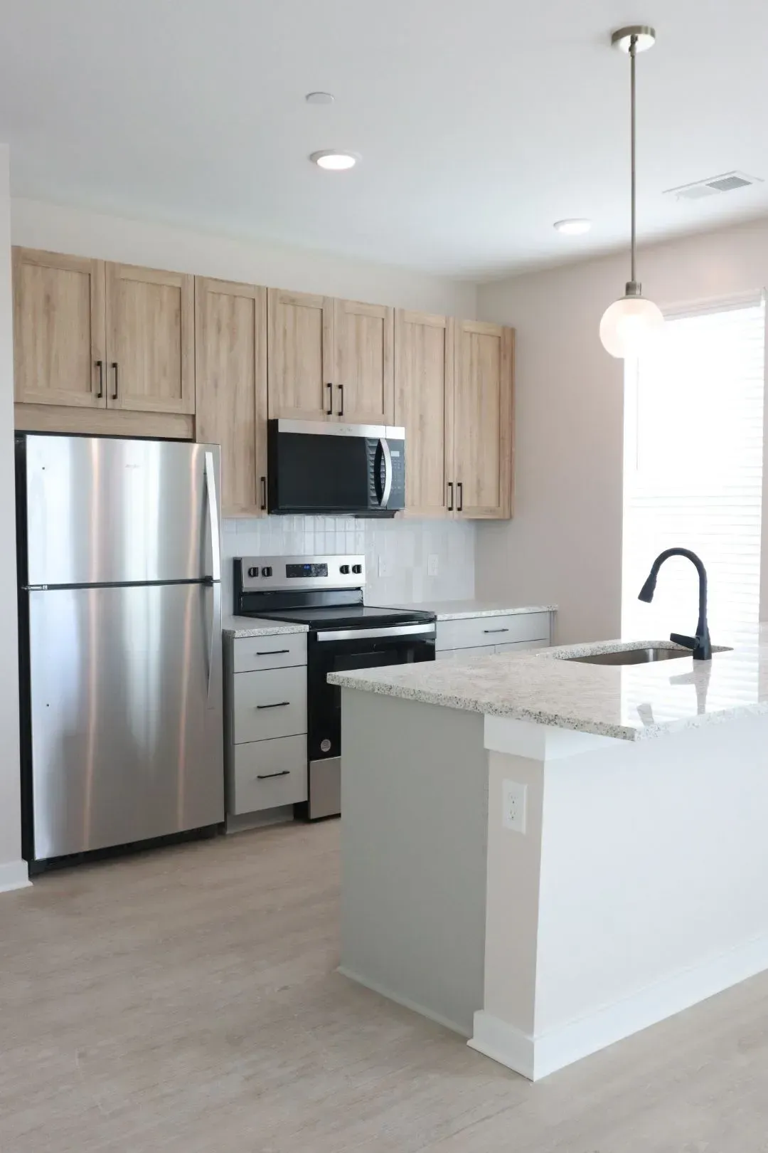 Modern apartment kitchen with stainless steel fridge, oven, microwave, and a white granite island.