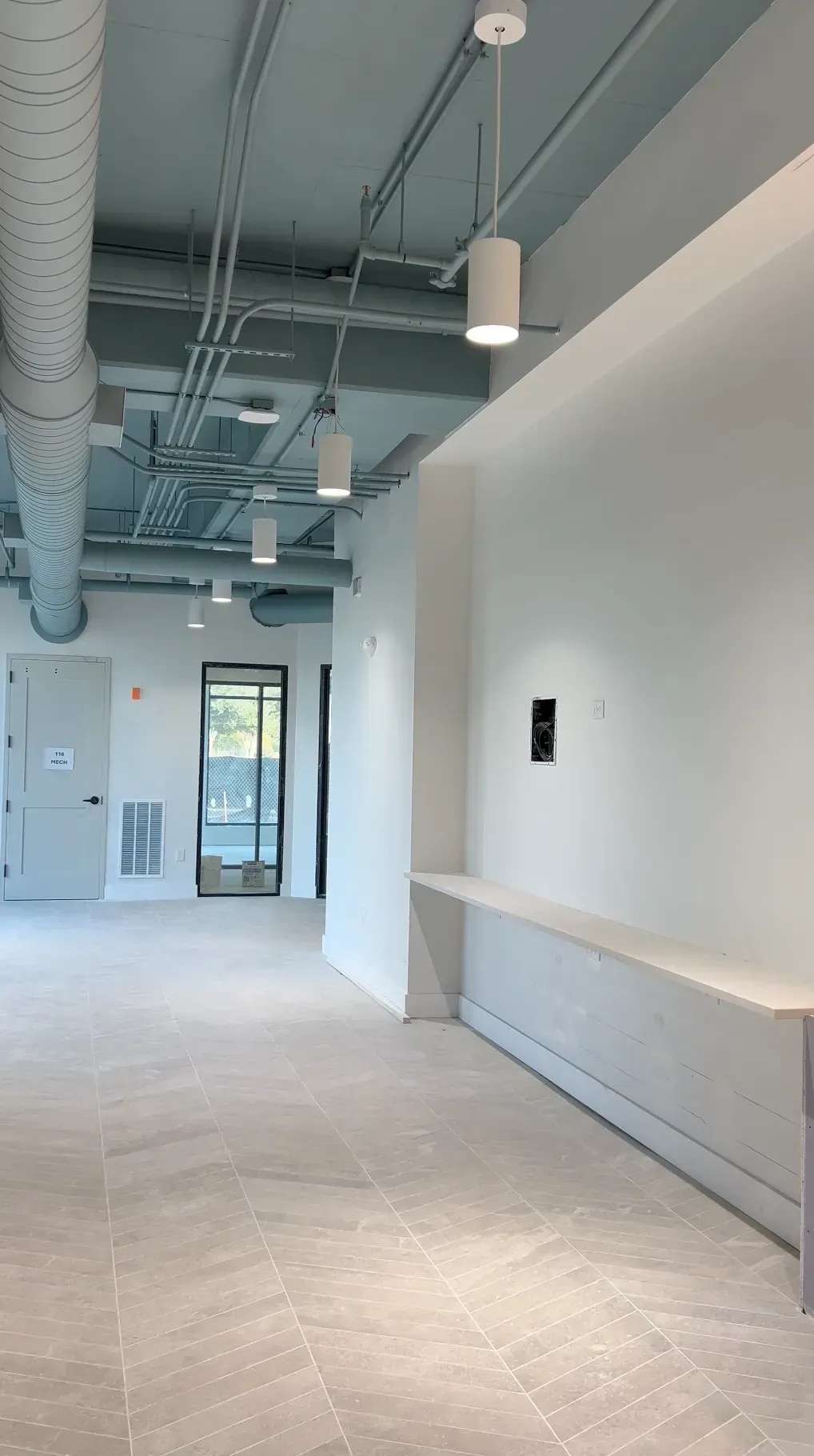 Interior community space with exposed ducts, white walls, pendant lights, and a long counter along the wall.