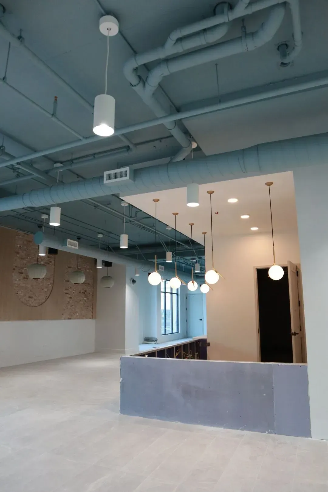 Industrial interior with exposed pipes and hanging pendant lights in a community space.