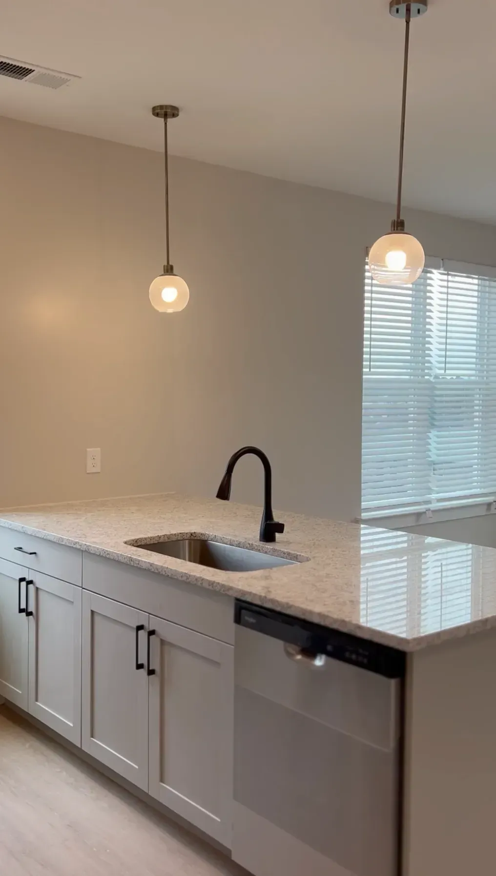 Modern kitchen with an island, speckled countertop, undermount sink, black faucet, and pendant lights.