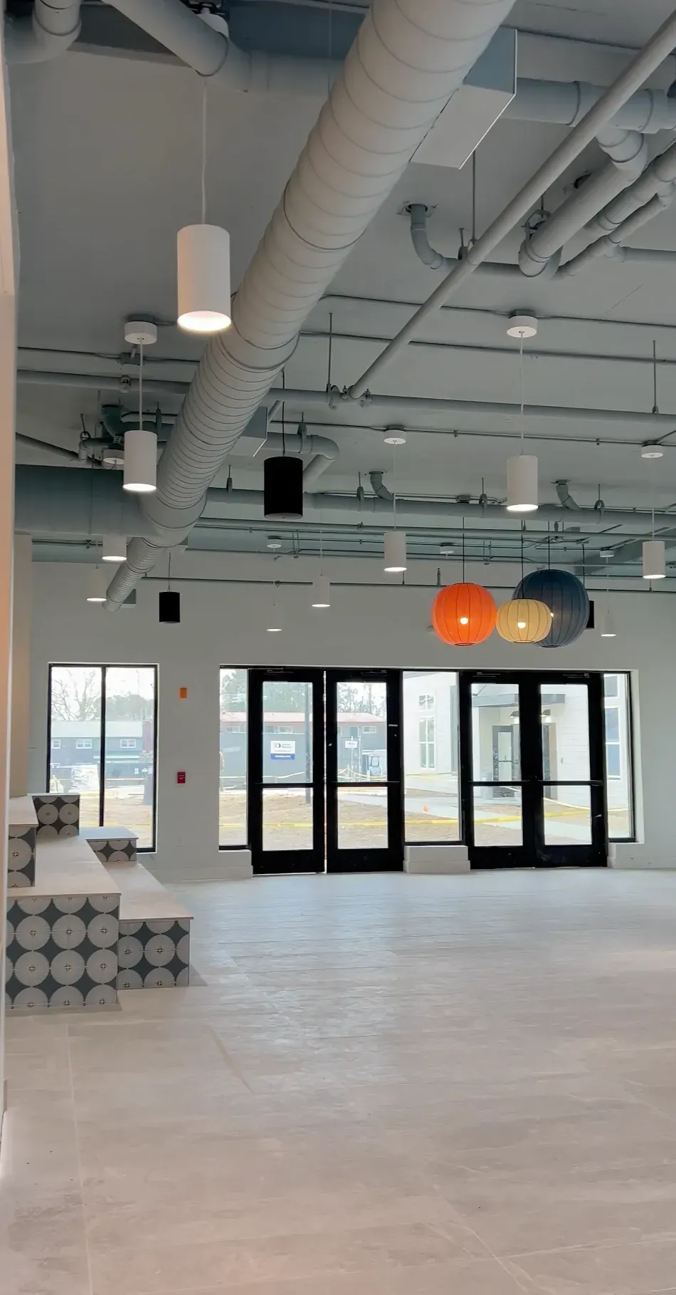 Interior lobby area with large glass entry doors, exposed ducts, and pendant lights.