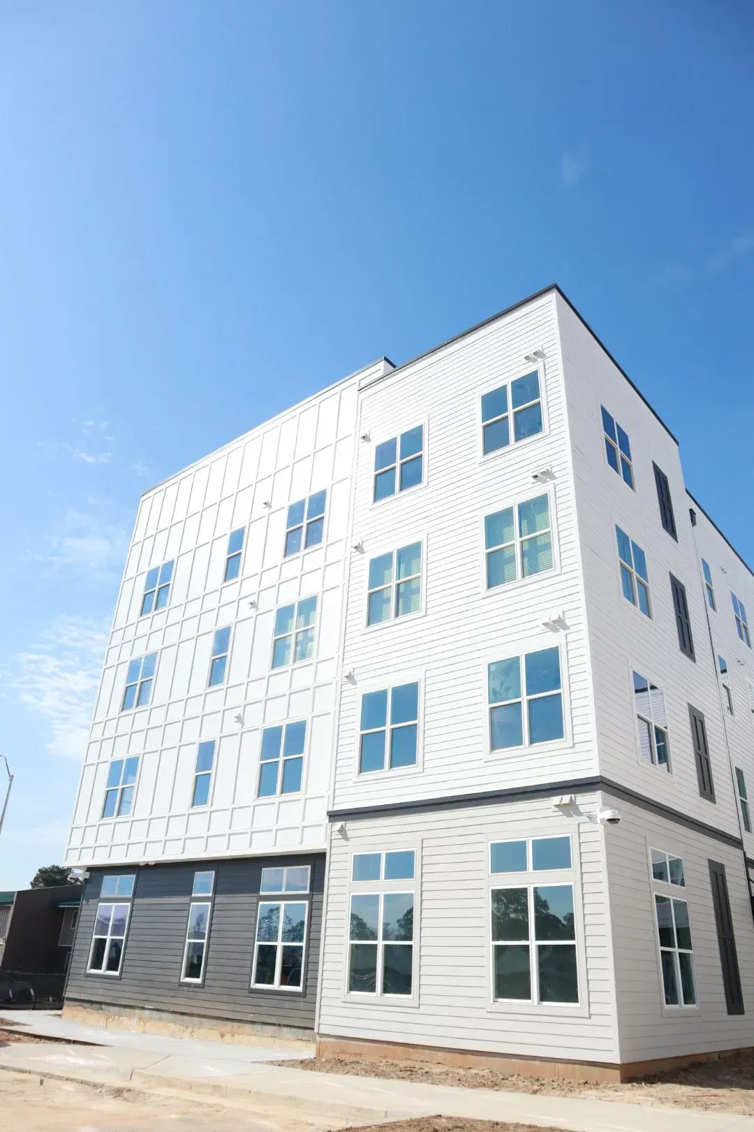 Exterior view of a white, modern, multi-story apartment building with numerous windows against a blue sky.