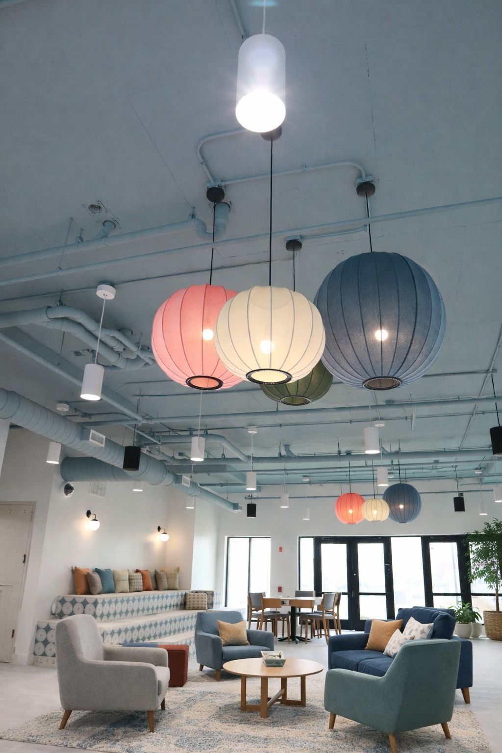 A modern lounge area with colorful spherical pendant lights, armchairs, and a built-in bench under a blue industrial ceiling.