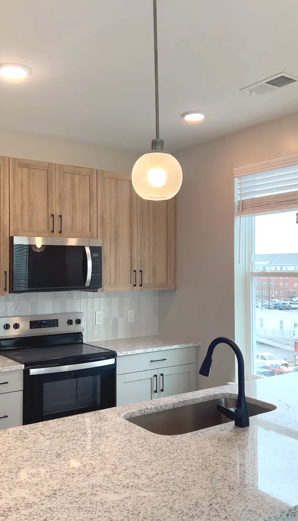 Modern kitchen with granite countertops, light wood cabinets, stainless steel appliances, and a window.