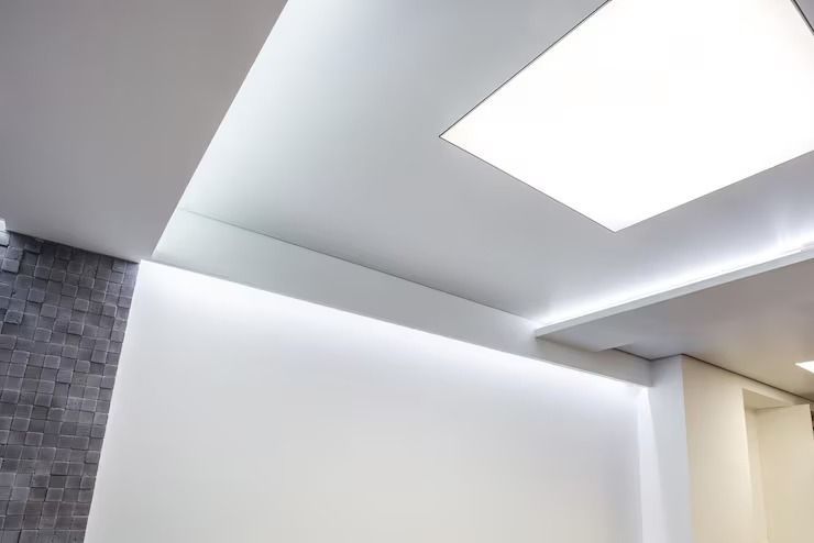 Modern interior ceiling with recessed lighting and a bright skylight above a white wall