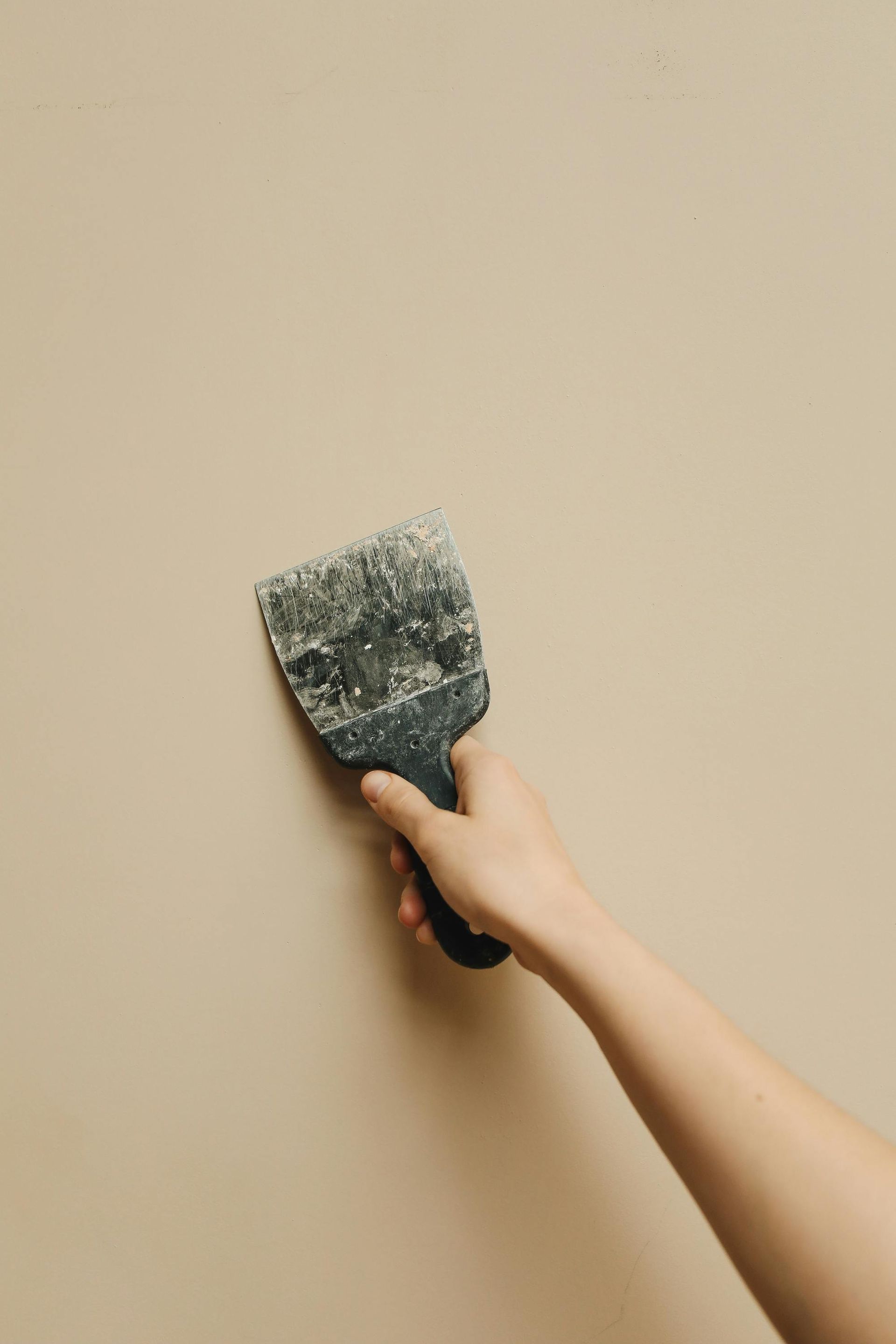 Hand scraping paint from a beige wall with a putty knife