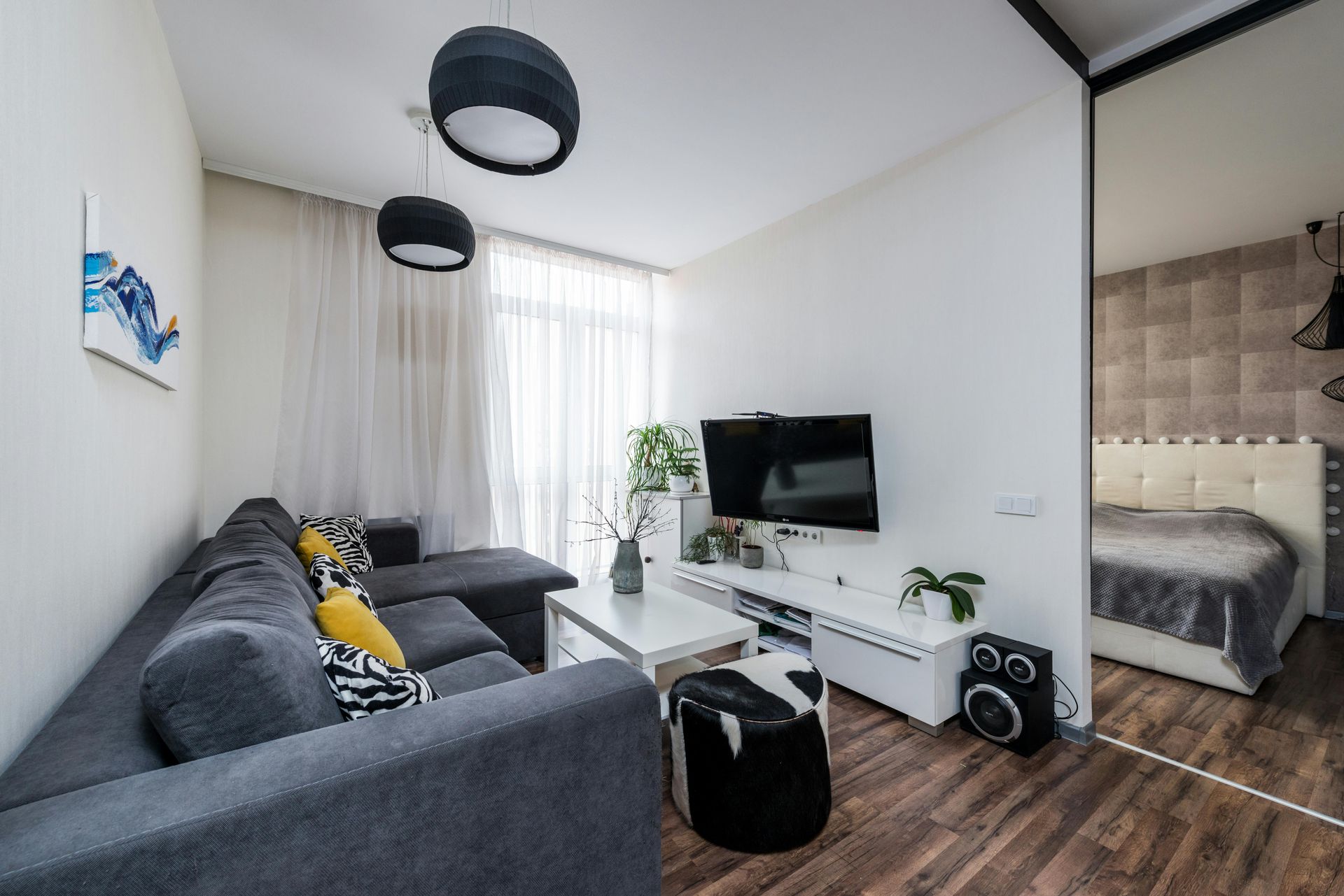 Modern living room with gray sectional sofa, wall-mounted TV, and a bedroom visible through an open doorway