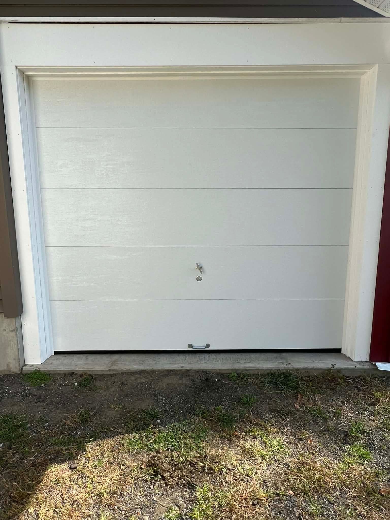 White garage door on a concrete foundation with grass in front.