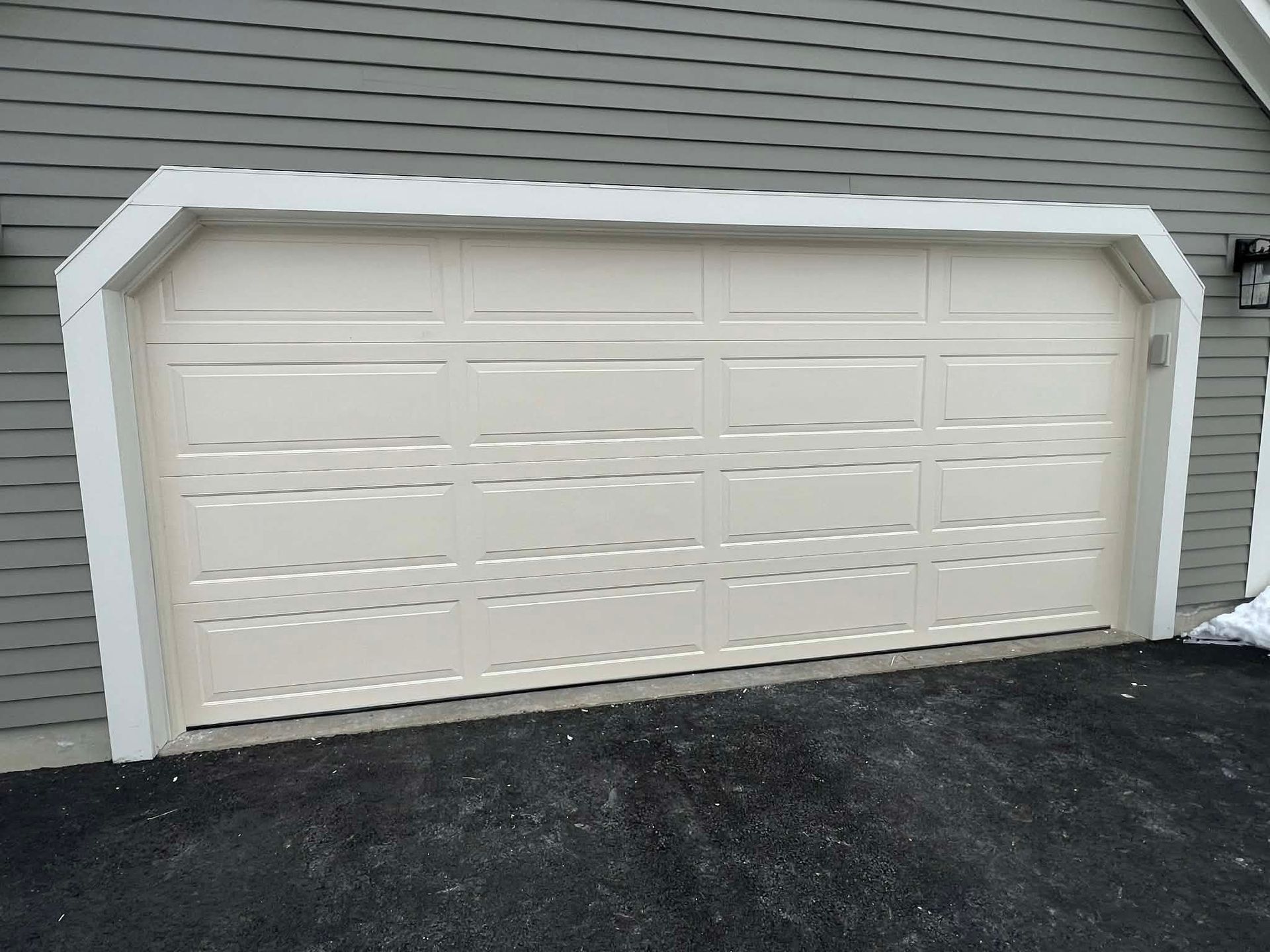 Beige garage door with white trim, set in front of gray siding.
