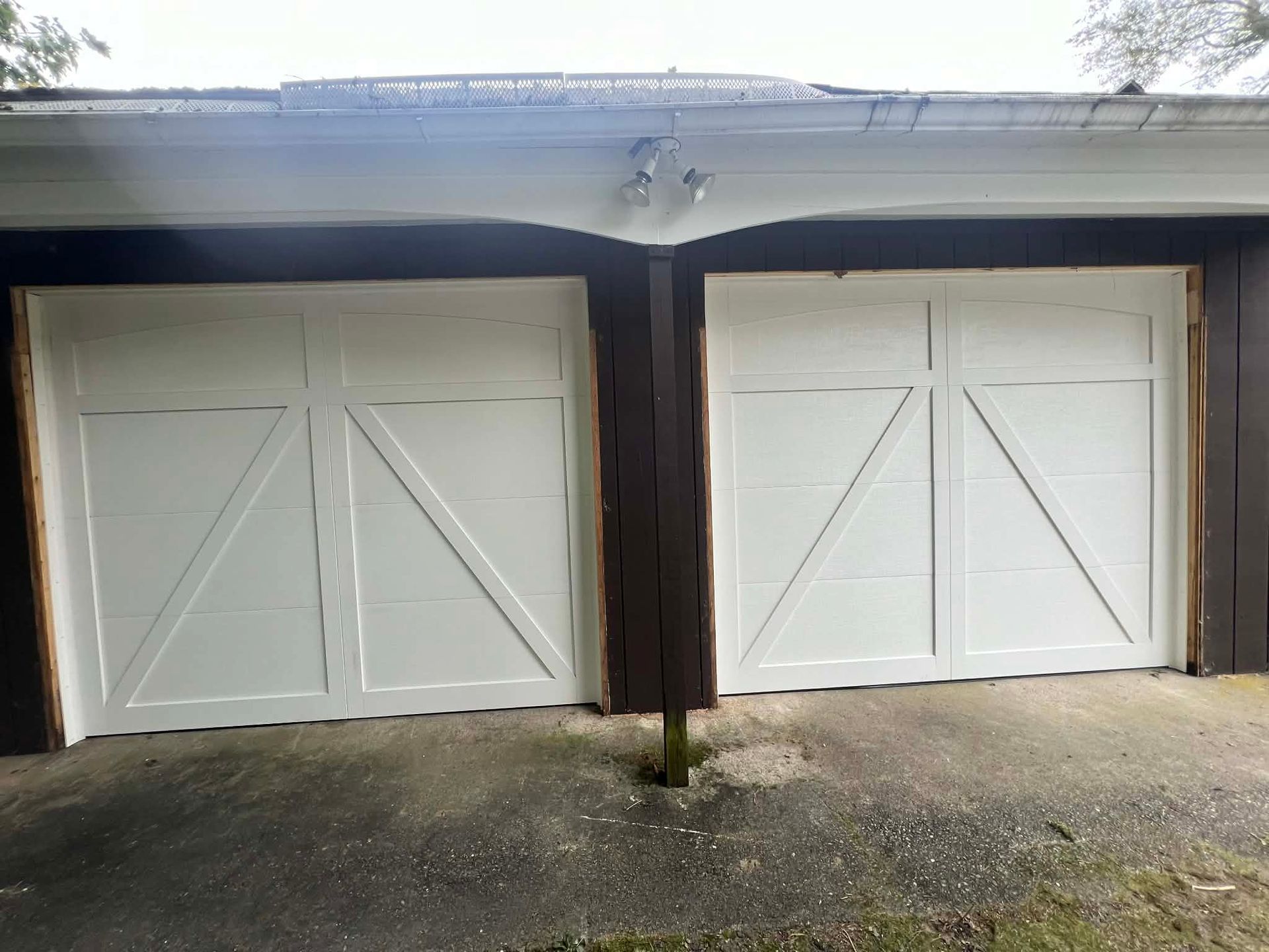White garage doors with dark brown trim, set in concrete, under a brown roof.